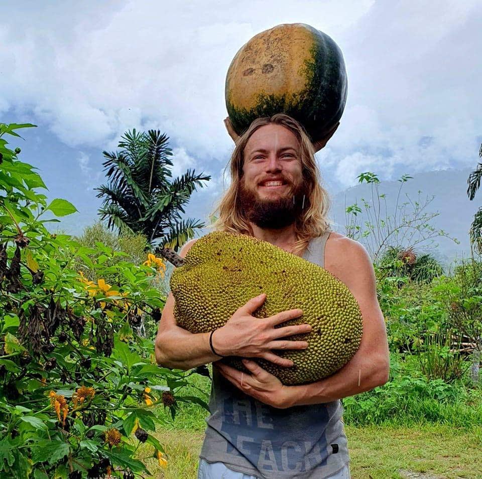 Osoba držící obrovský jackfruit a dýni nad hlavou.